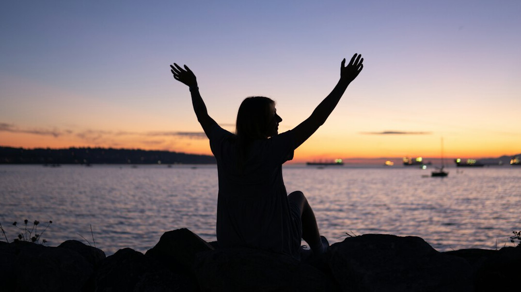 Woman relaxing outdoors with arms raised at sunset